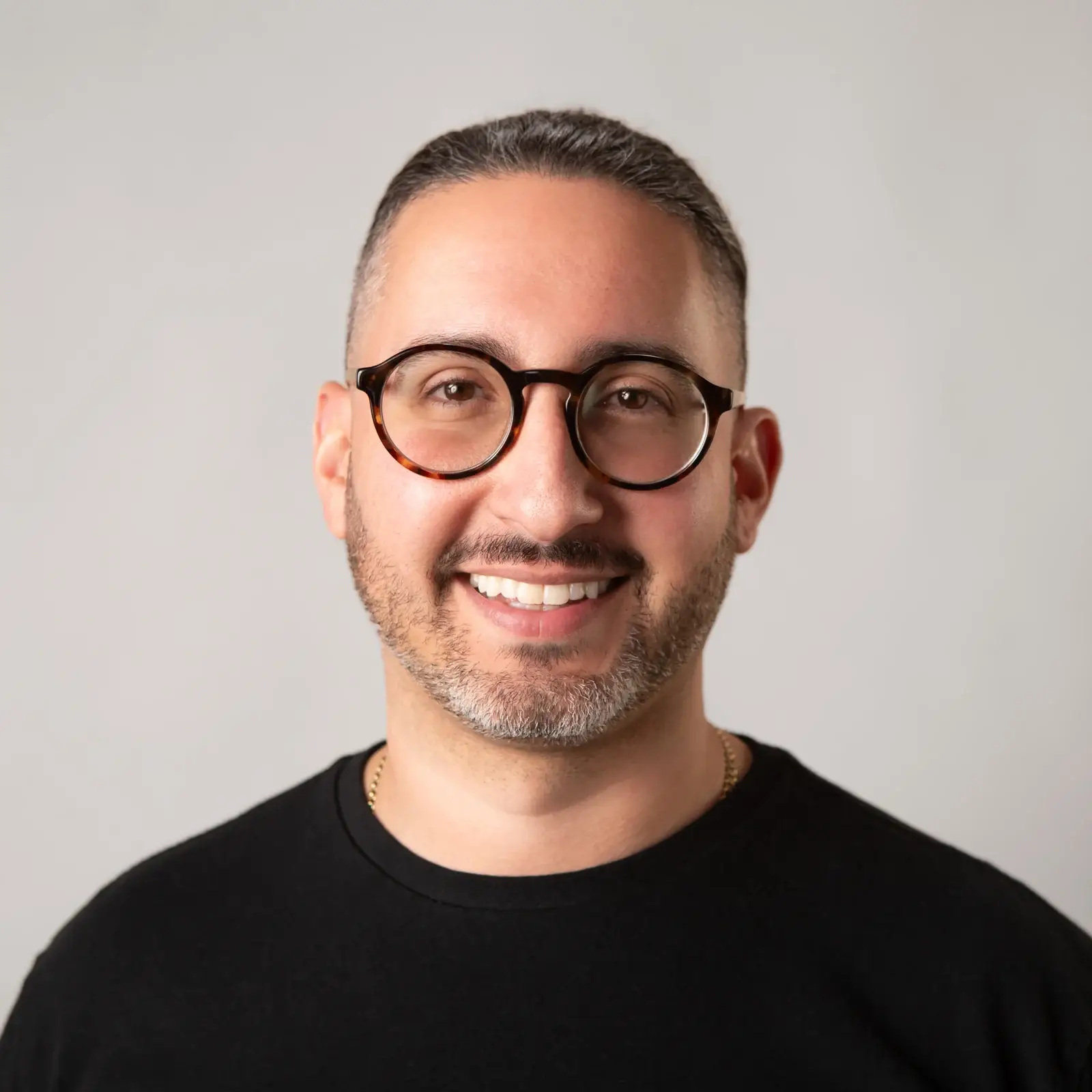 Greg Petrossian, AI advisor, smiling in a black tee and glasses